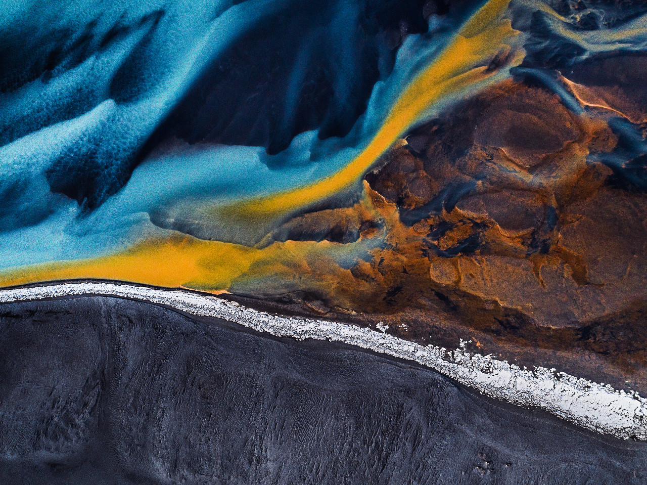Aerial shot looking down on a braided river at the edge of a black sand beach